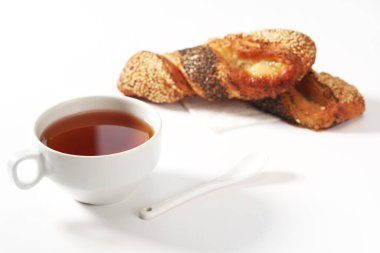 Beyaz arka planda tohumlu lezzetli çöreklerle bir fincan sıcak çay.