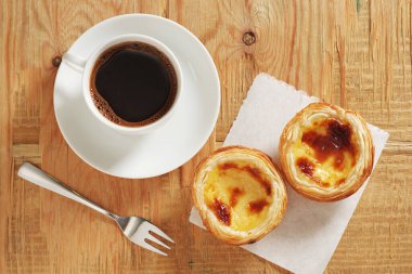 Pastel de nata 'nın ve eski ahşap arka planda bir fincan kahvenin tam üstünde.