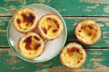 Eski yeşil ahşap arka plandaki bir tabağın üzerindeki pastel de nata pastası manzarasının hemen üstünde.