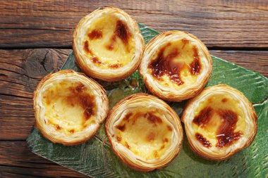 Masanın üzerinde yeşil seramik bir tahta üzerinde Pastel de Nata, üst manzara. Geleneksel Portekiz hamur işi