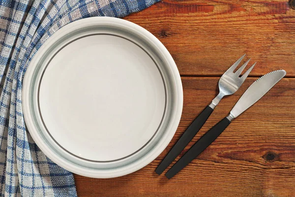 Empty clean plate with cutlery on dark wooden table, top view