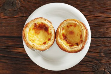 Pastel de nata pastasının hemen üstünde, ahşap arka plandaki bir tabakta, üst manzara.