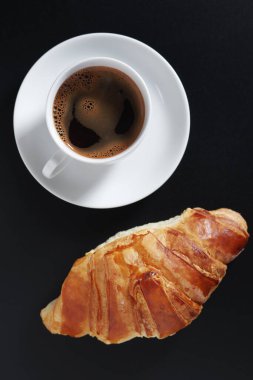 Siyah arka planda kruvasan ve bir fincan kahve.