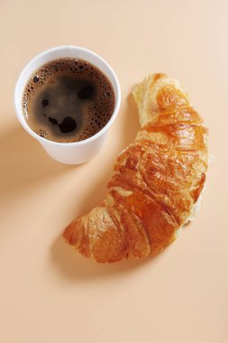 Kruvasan ve bej arka planda kahve olan tek kullanımlık kağıt bardak. Paket yemek.