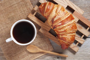 Bir fincan kahve ve kruvasan, ahşap masa, üst manzara.