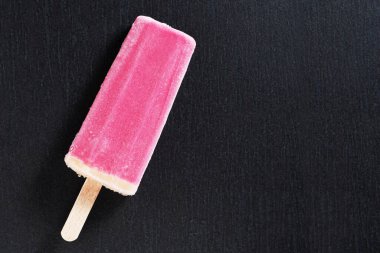 Popsicle on stick on black stone background, top view with copy space