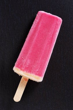 Ice cream on stick on black stone background, top view