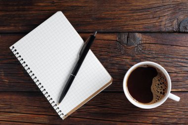 Notepad with pen and a cup of coffee on wooden background, top view