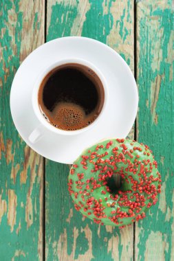 Donut with green icing and cup of coffee on old wooden background, top view