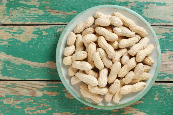 Peanuts on a plate on old green wooden background, top view with copy space