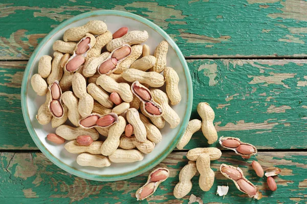 Peanuts on a plate on old green wooden background, top view