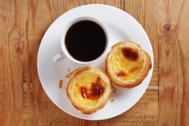 Tipik Portekiz pastel de nata yumurtası turtası. Eski ahşap arka planda bir tabakta bir fincan kahve, üst manzara.