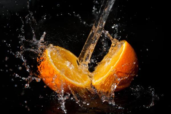 Meia laranja com salpicos de água em um fundo preto — Fotografia de Stock