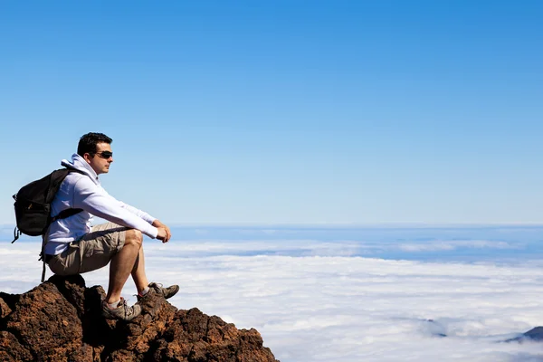 Молодой человек отдыхает на высоком пике над облаками — стоковое фото