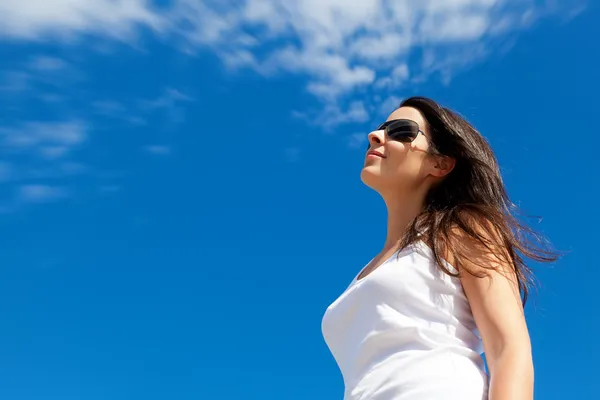 Молода жінка, посміхаючись на фоні синього неба — стокове фото