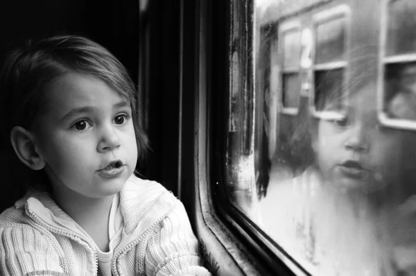 小さな女の子は窓の反射を見るします。彼女は電車を旅します。. — ストック写真