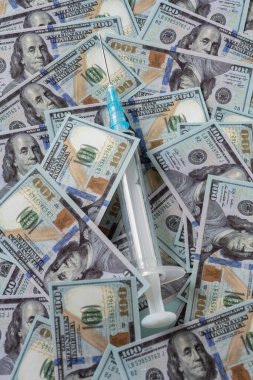 Dolar yığınında bir enjektör. Aşı veya uyuşturucudan kâr elde etme kavramı.