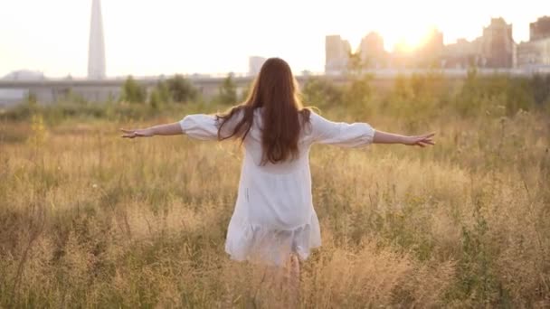 Girl walks across a sunny field in a white dress and turns into camera — Vídeo de Stock