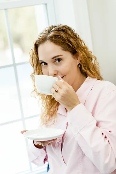 Mujer relajándose junto a la ventana con bebida — Foto de Stock