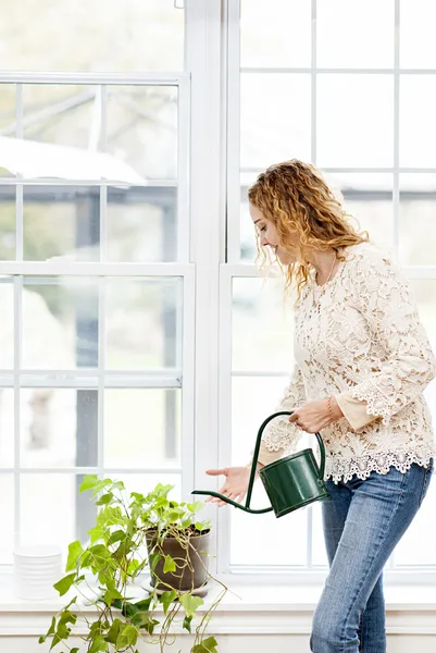 Sorrindo mulher regando planta em casa — Fotografia de Stock