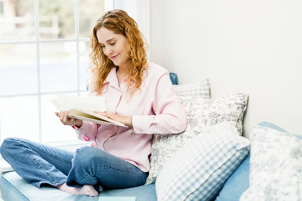 Kvinna läsa bok av fönster — Stockfoto