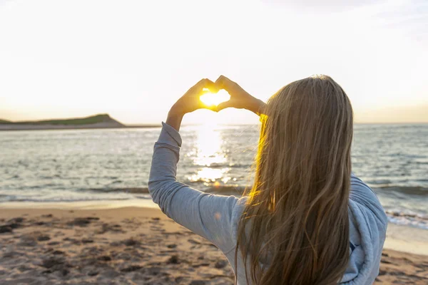 Flicka håller hand i hjärtat form på stranden — Stockfoto