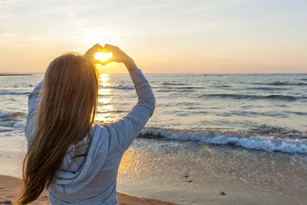 Flicka håller hand i hjärtat form på stranden — Stockfoto