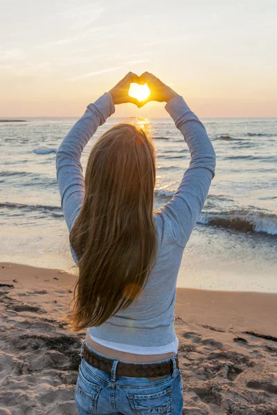 Girl holding hands in heart shape at beach — Stock Photo, Image