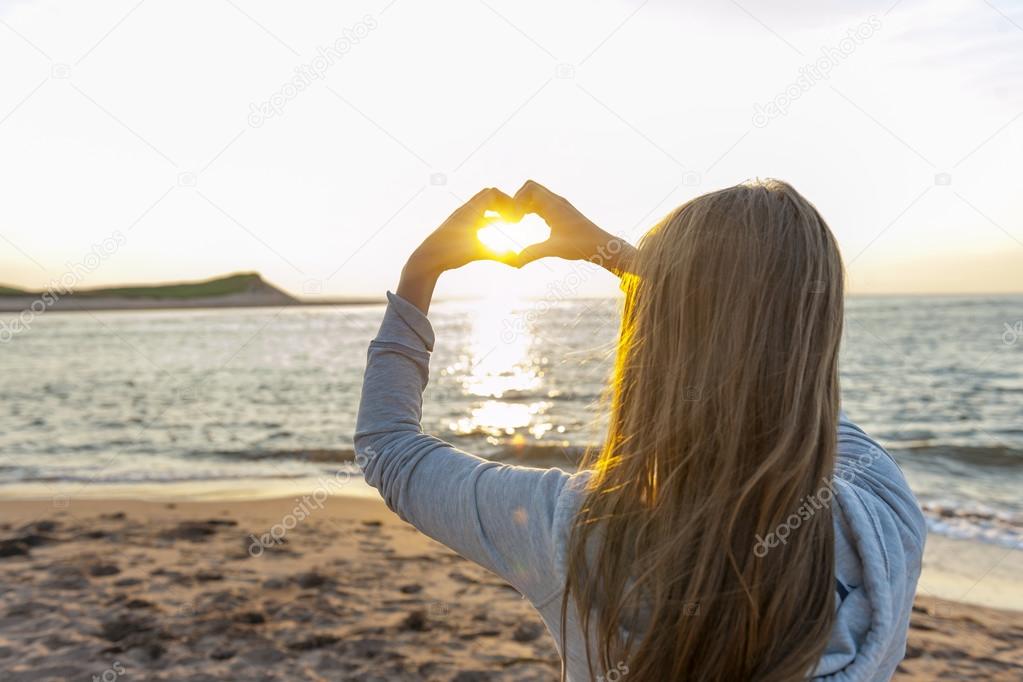 Girl holding hands in heart shape at beach