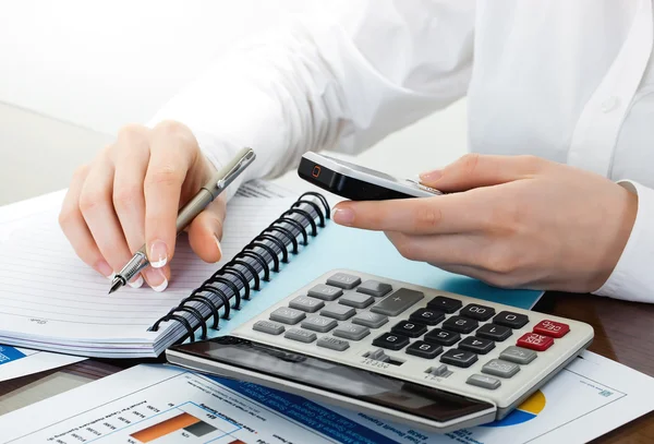 Manos sosteniendo el lápiz y presionando los botones de la calculadora sobre documentos — Foto de Stock