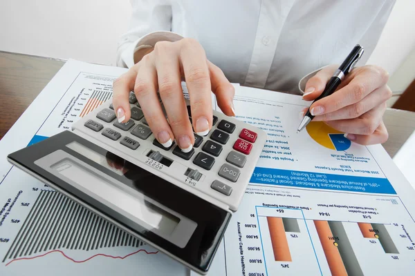 Hands holding pencil and pressing calculator buttons over documents — Stock Photo, Image