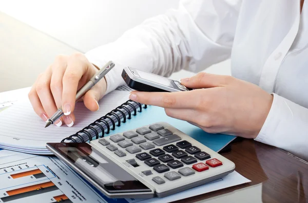 Manos sosteniendo el lápiz y presionando los botones de la calculadora sobre documentos — Foto de Stock