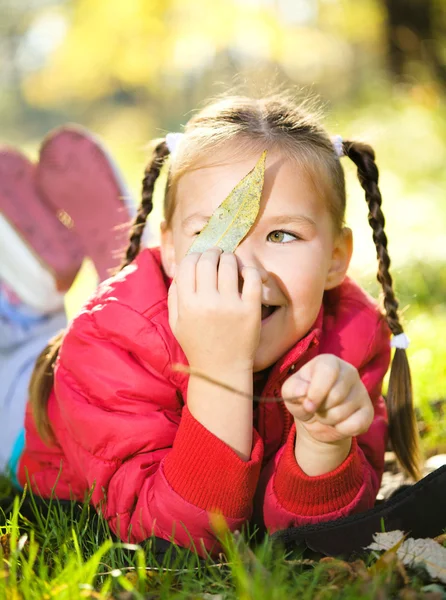 Nettes kleines Mädchen spielt mit Blättern im Park — Stockfoto