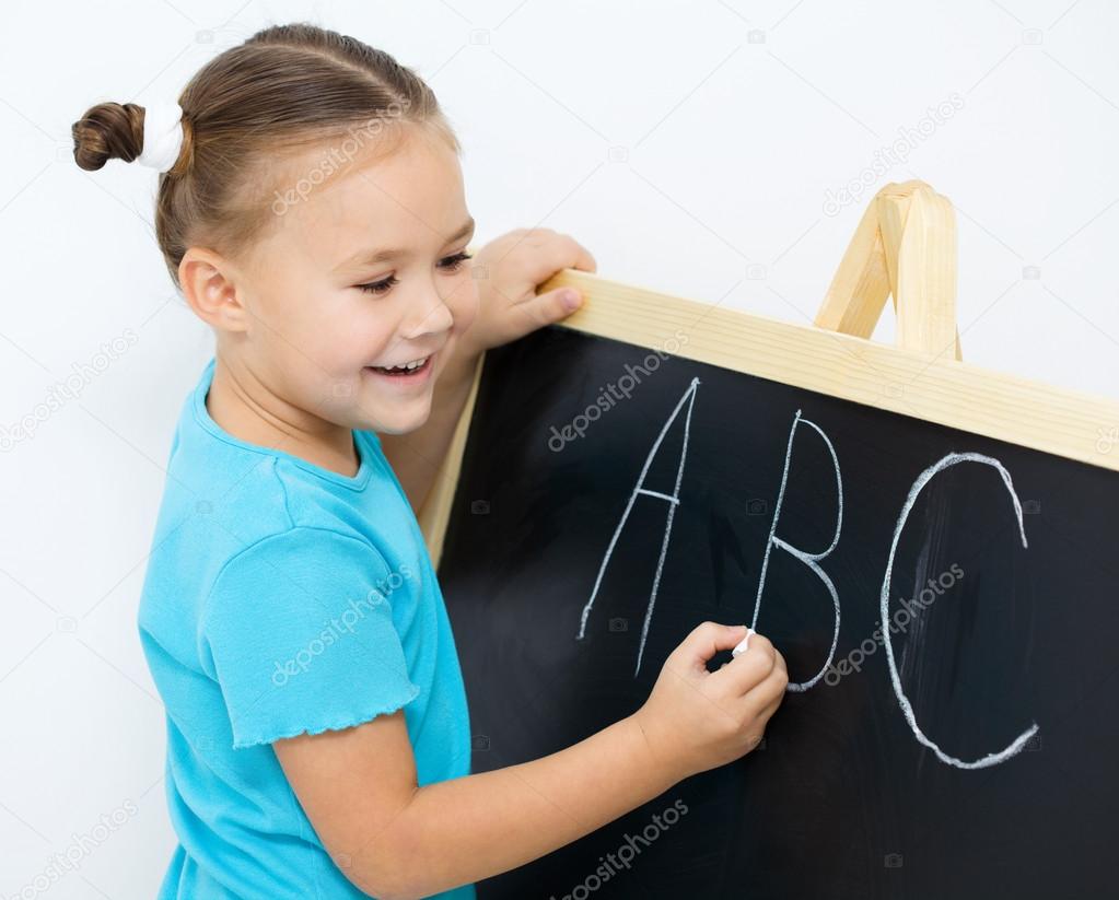 Little girl is writing letters on a blackboard