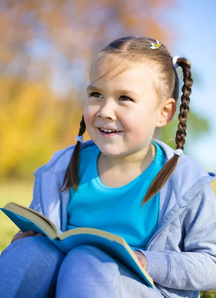 Little girl is reading a book outdoors — Stock Photo, Image