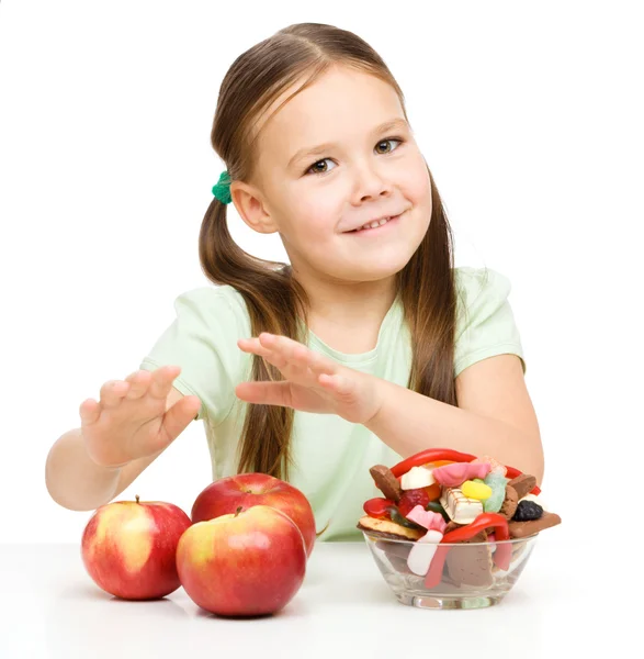 Маленькая девочка выбирает между яблоками и сладостями — стоковое фото