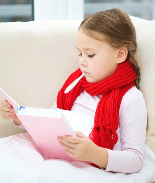 Nemocná holčička s teploměrem čte knihu — Stock fotografie