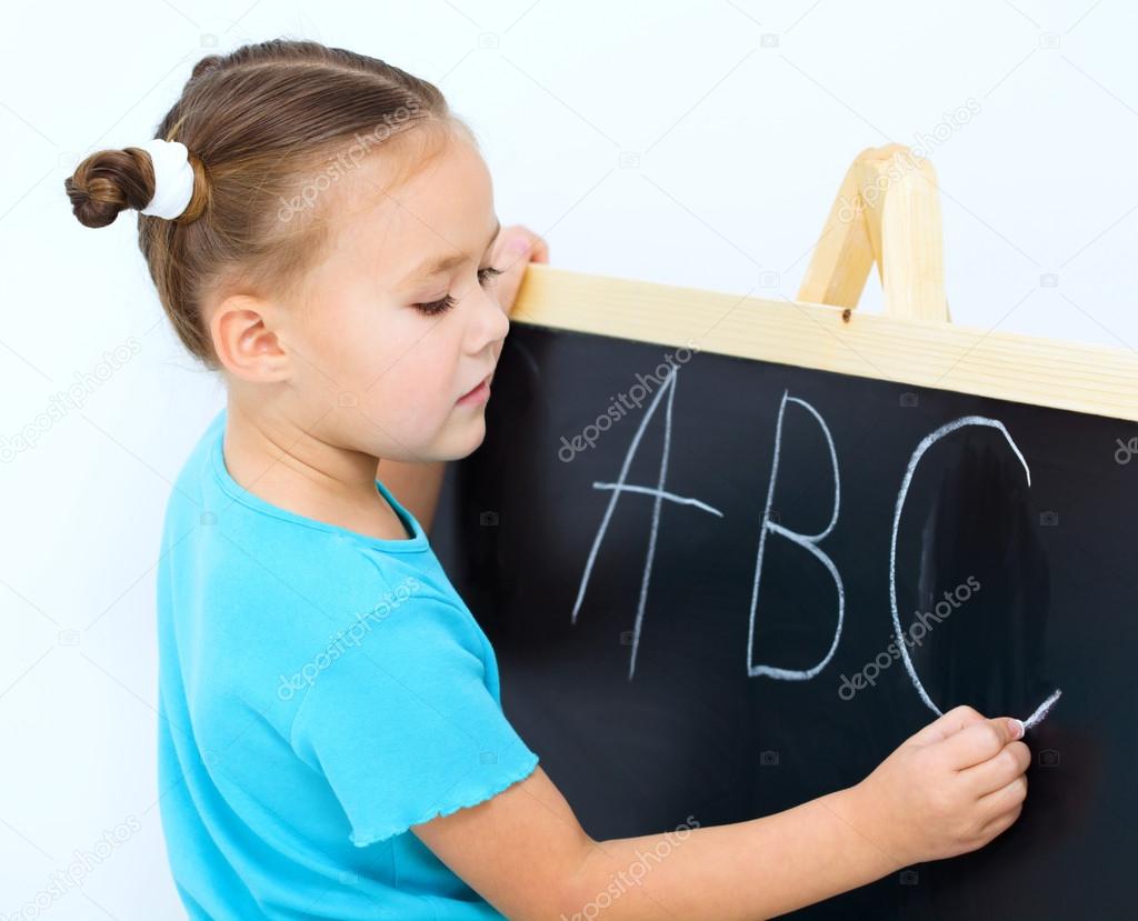 Little girl is writing on a blackboard