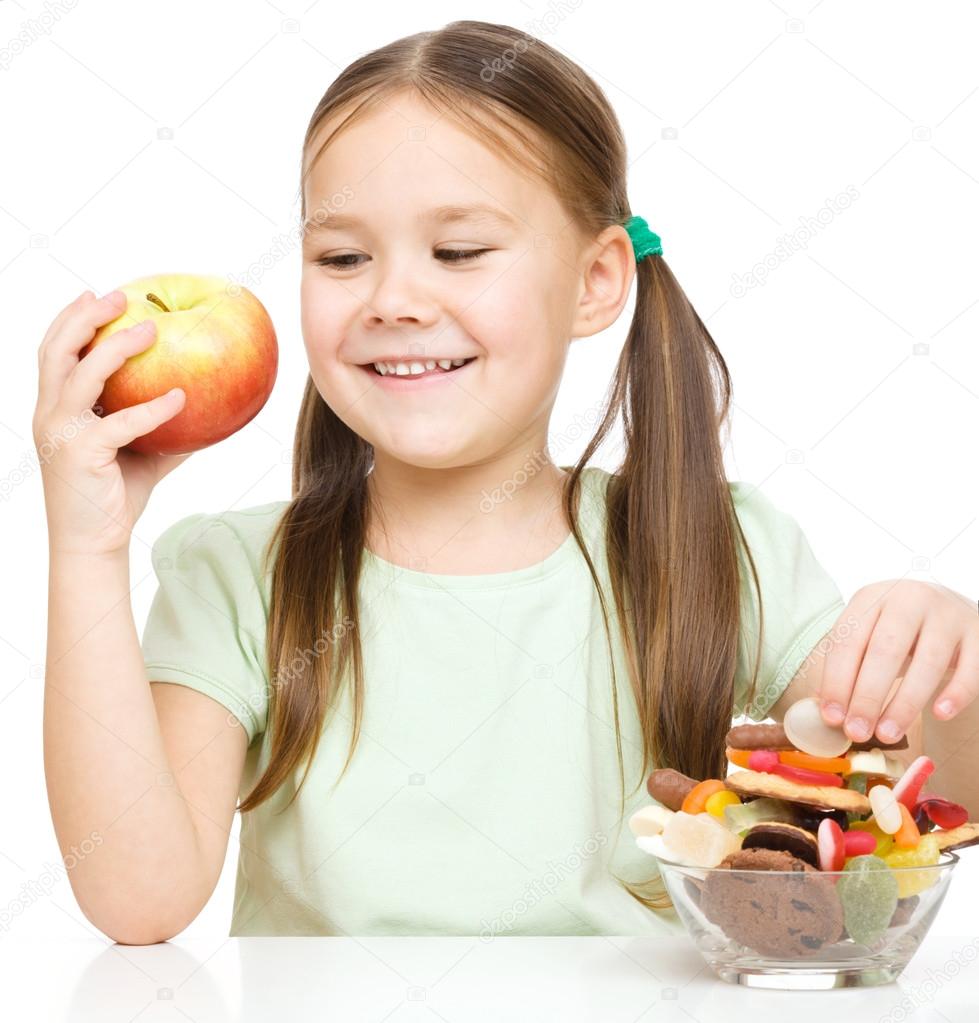 Little girl choosing between apples and sweets