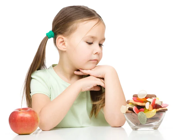 Little girl choosing between apples and sweets — Stock Photo, Image