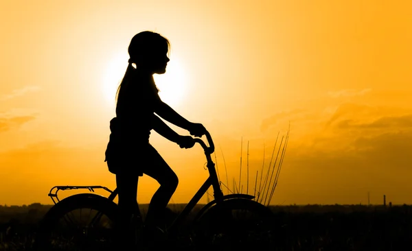 Silhueta de menina pequena em uma bicicleta — Fotografia de Stock