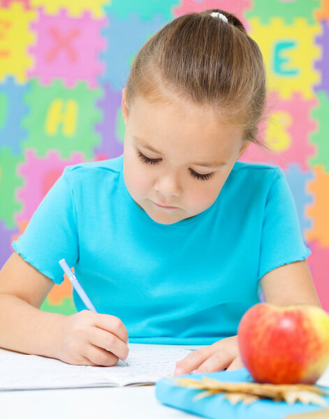 Маленькая девочка пишет ручкой.
