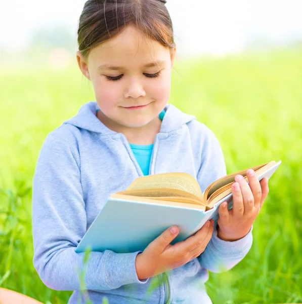 Little girl is reading a book outdoors — Stock Photo, Image