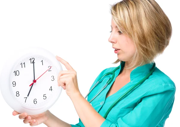 Junge Ärztin hält Uhr, die sieben zeigt — Stockfoto