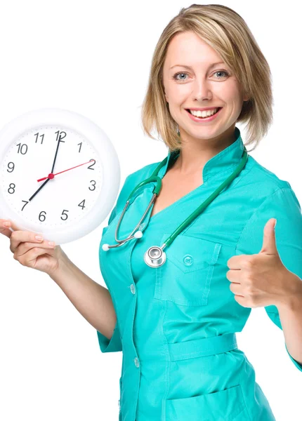 Jovem doutora está segurando relógio mostrando sete — Fotografia de Stock