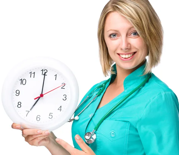 Jeune femme médecin tient horloge montrant sept — Photo