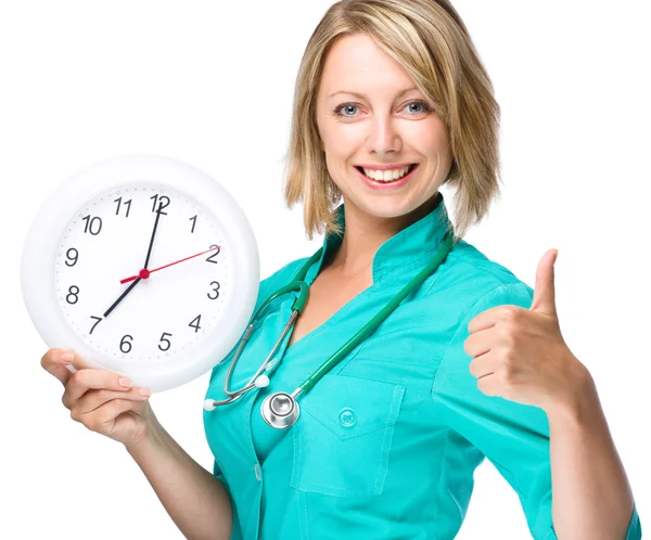 Jeune femme médecin tient horloge montrant sept — Photo