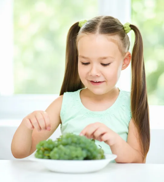 Cute little girl is eating green grapes — Stock Photo, Image