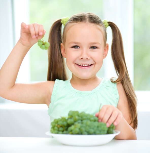 Cute little girl is eating green grapes