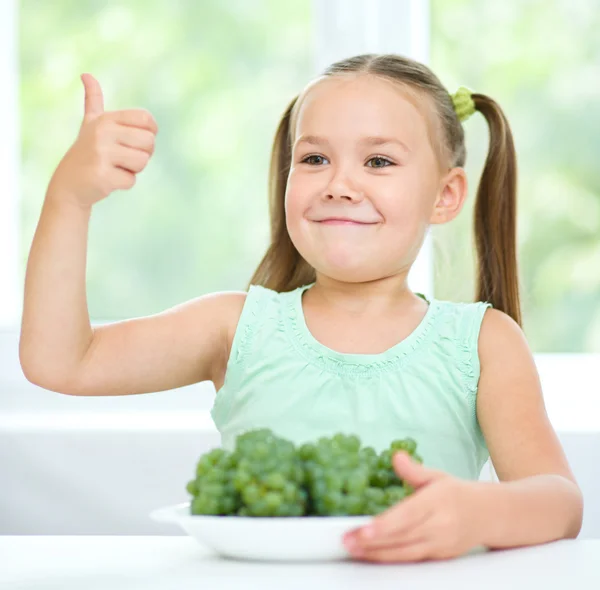 Cute little girl is eating green grapes — Stock Photo, Image